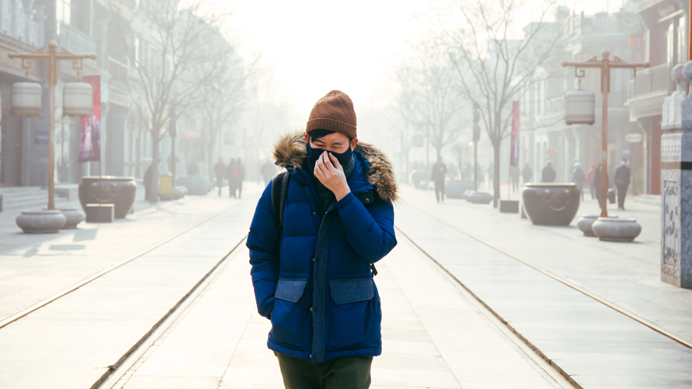 An image of a man in China covering his face as he walks down the street