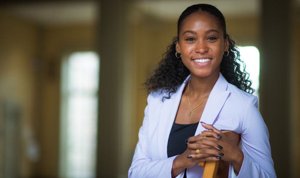 Student Kendyll Hicks sitting with her hands crossed on the chair back and smiling at the camera