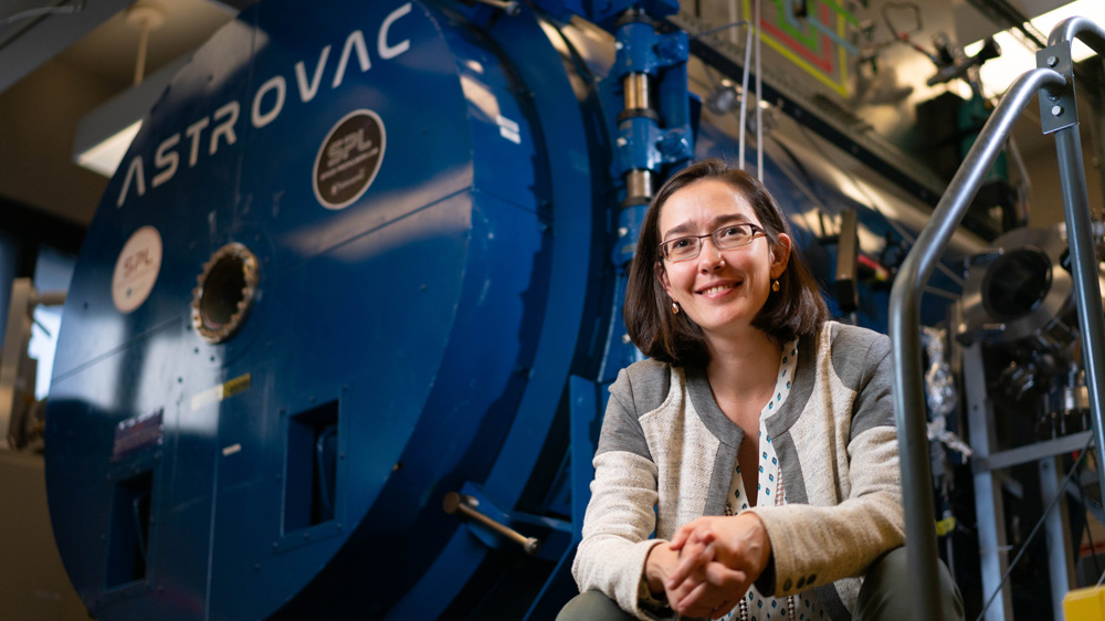 Carmen Guerra-Garcia sitting in a lab next to a large blue vacuum chamber