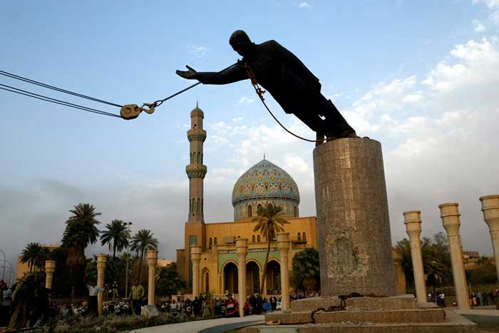 Photo of statue of Saddam Hussein being removed, with a mosque and people in background 
