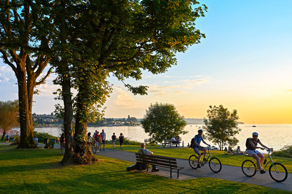 People ride bikes and relax near a river on a gorgeous day