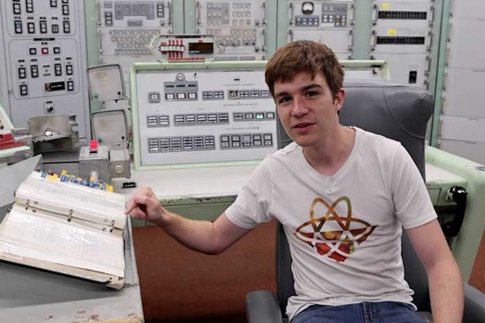James Dingley is in an old control room with lots of switches and buttons, and points to a large binder while talking to the camera