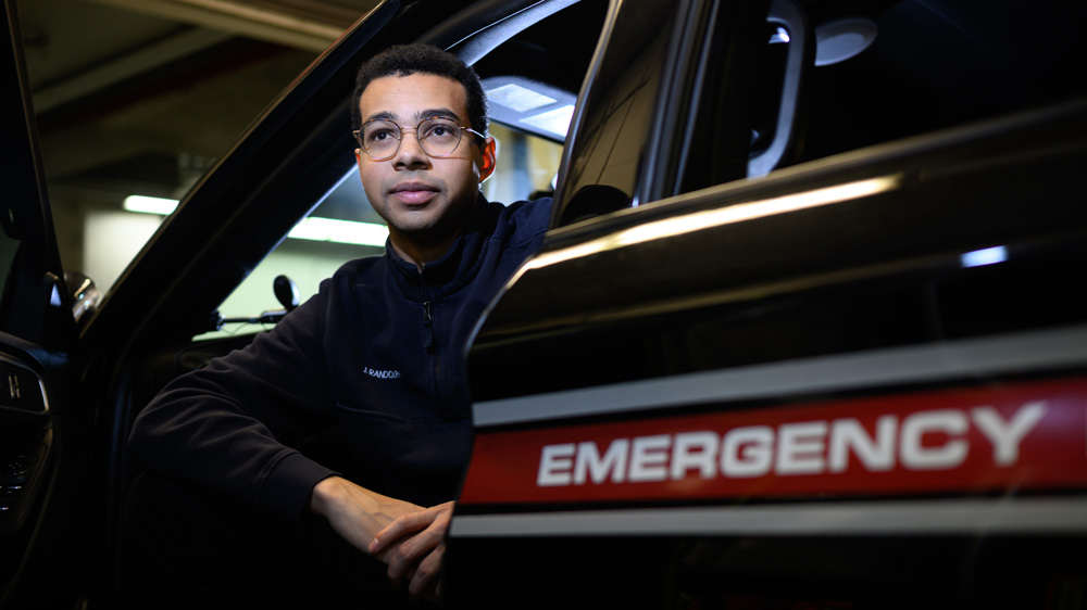 Josh Randolph sits in an EMS vehicle that says "emergency"