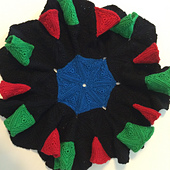 A crocheted afghan of equilateral triangles, joined seven at a vertex.  The center is blue, surrounded by a ring of black triangles.  The third ring of triangles alternates pairs of red triangles with triples of green, separated by triples of black.