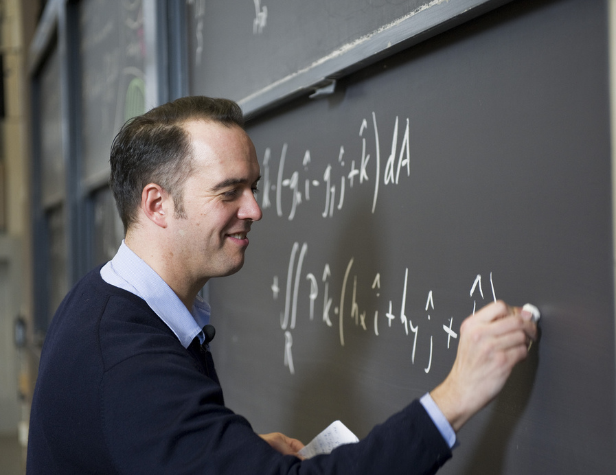 A professor writes an equation on a chalkboard.