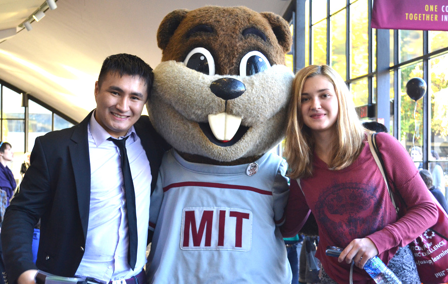 Two students stand on either side of the Tim the Beaver mascot, who is wearing a t-shirt with the letters MIT.