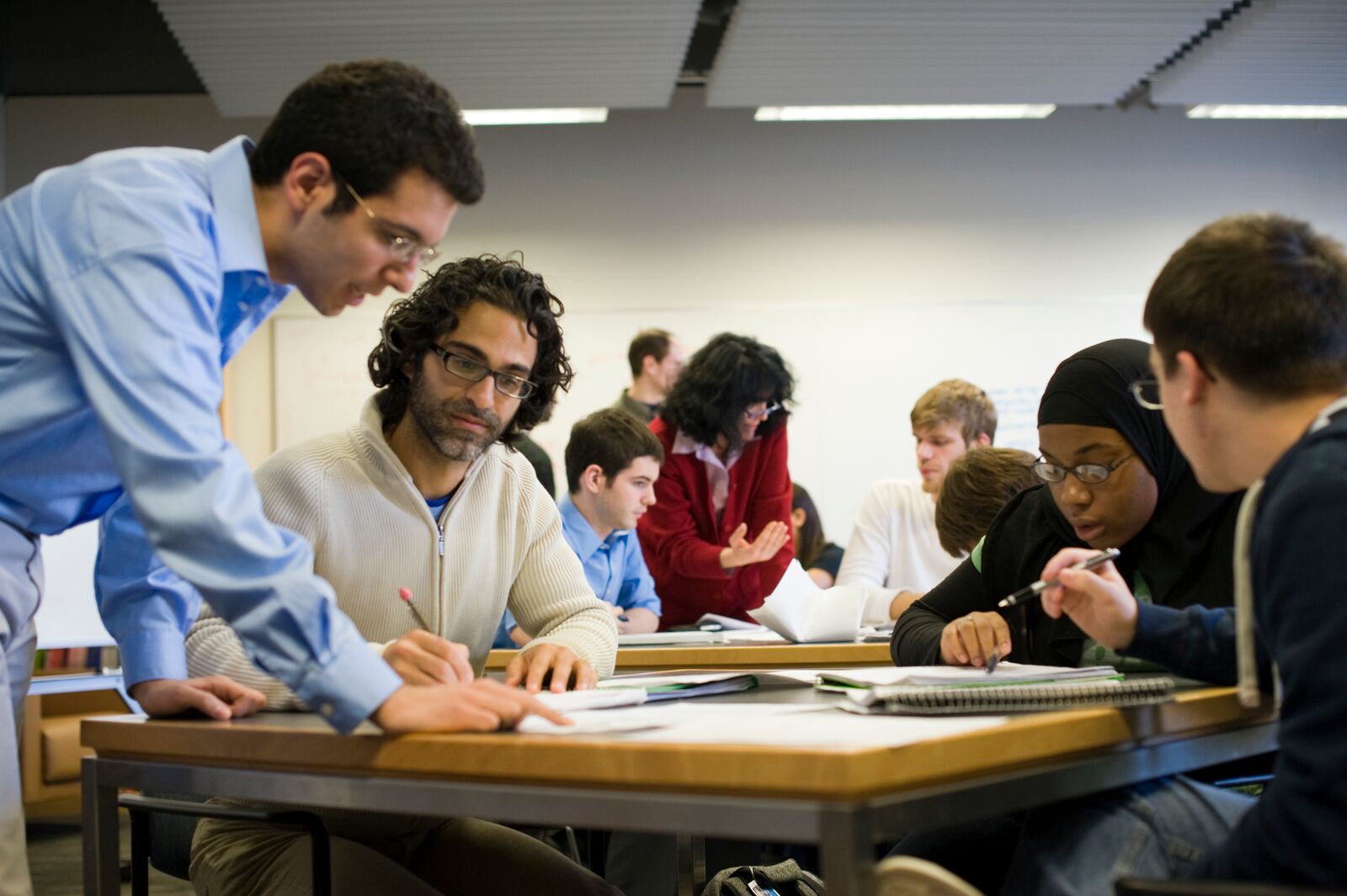 Students and instructors are gathered around several tables, speaking and interacting with one another.