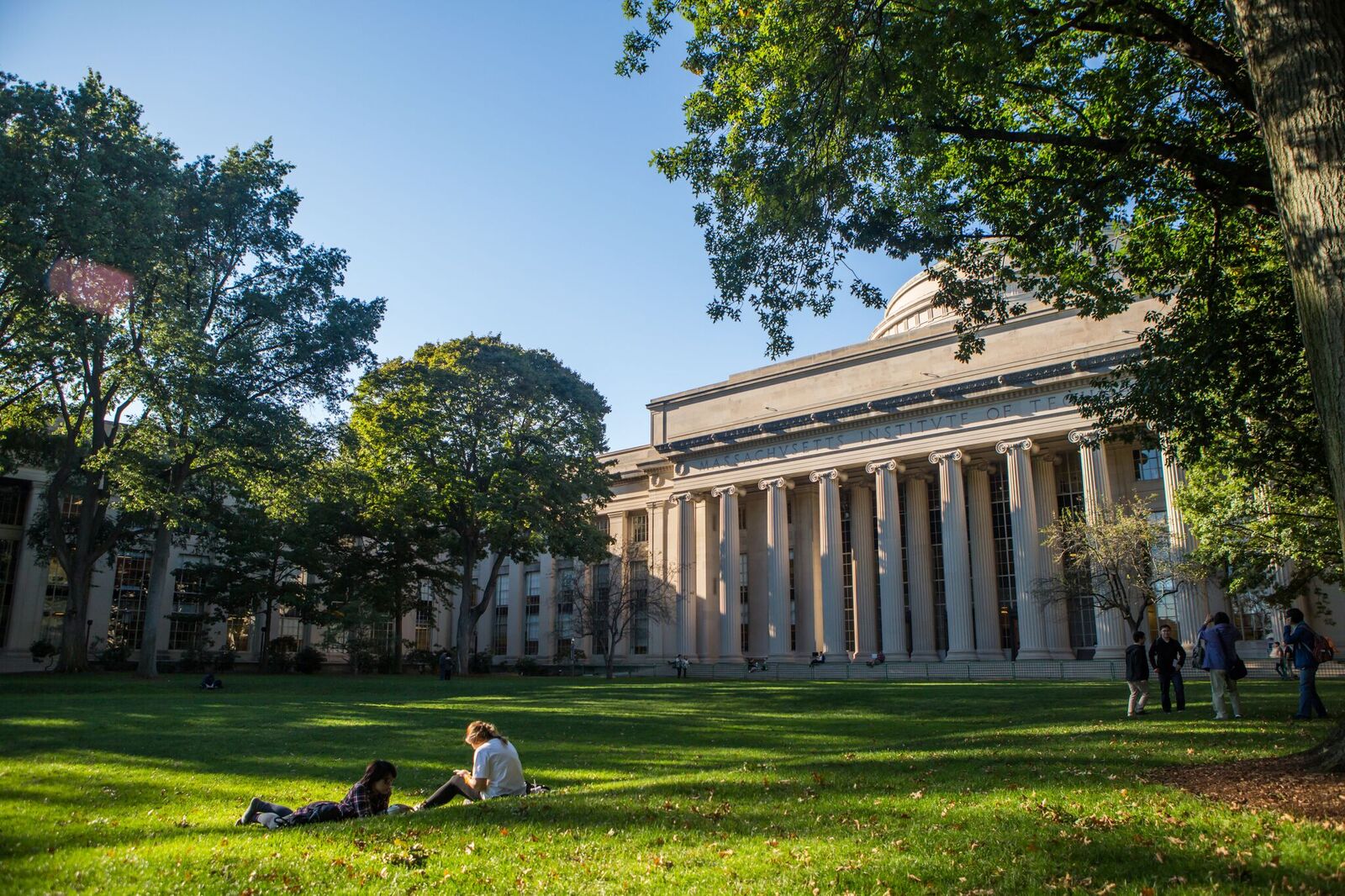 Two students on the grass in Killian Court. One is stretched out and the other is sitting up.