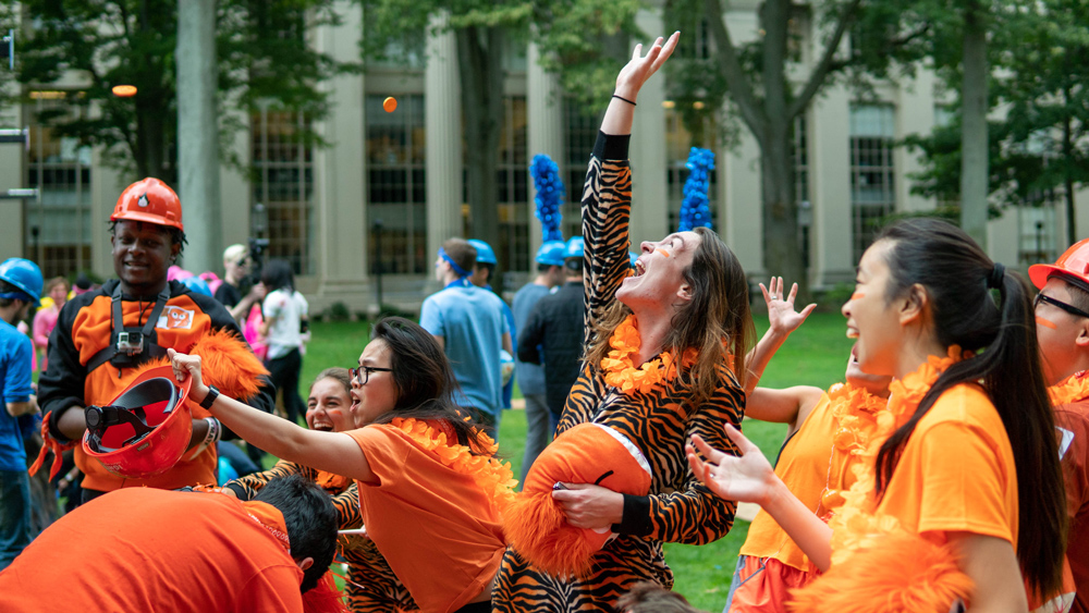 students dressed in bright orange trying to catch orange balls flying through the air