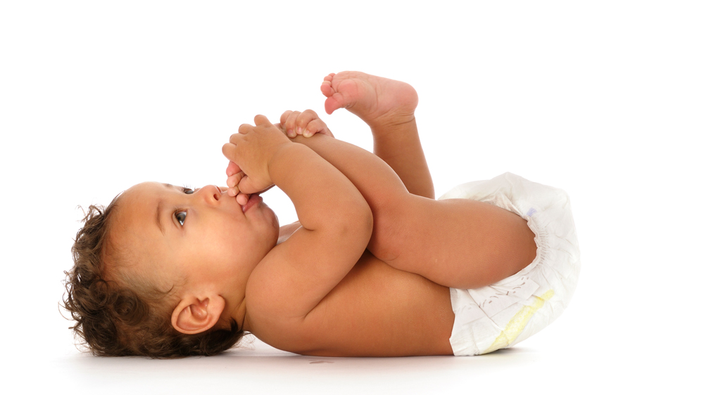 a baby, wearing a diaper, while lying on her back with her feet in the air