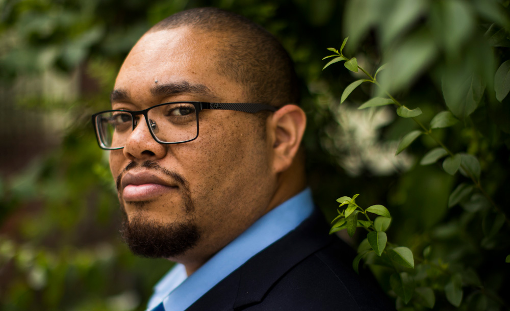 a closeup of Asegun Henry standing in front of greenery