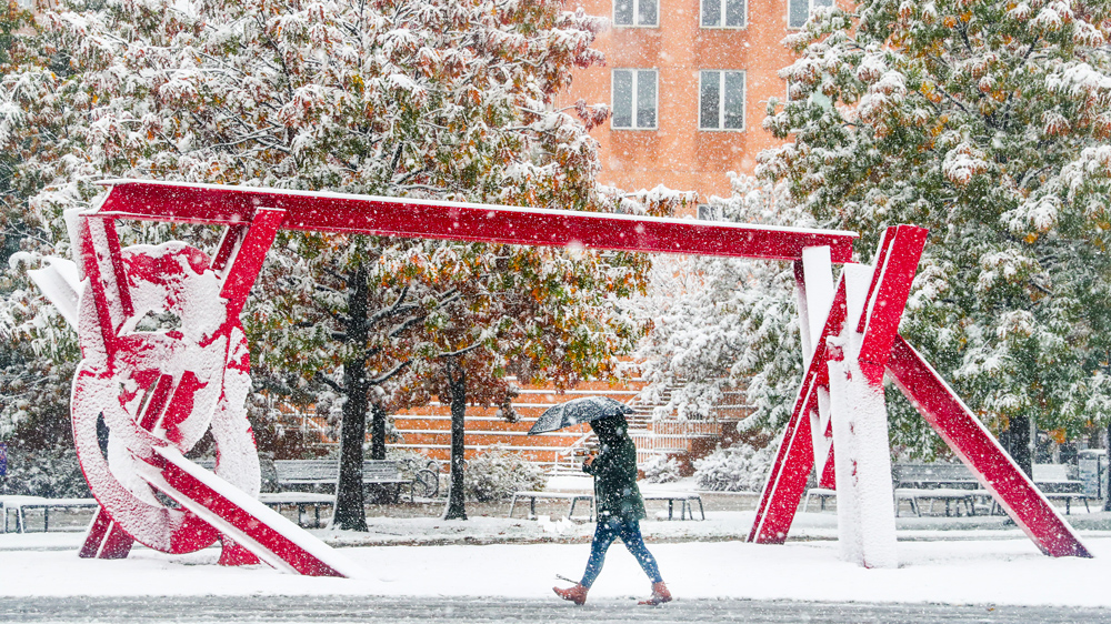 a lone person walks in front of a snow-covered red metal sculpture in Hockfield Court at MIT