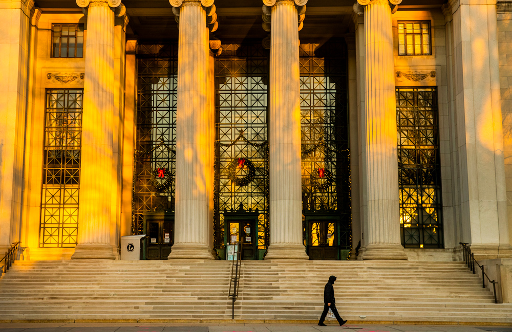 the columns and building front of MIT's main entrance bathed in golden light while a lone pedestrian walks by