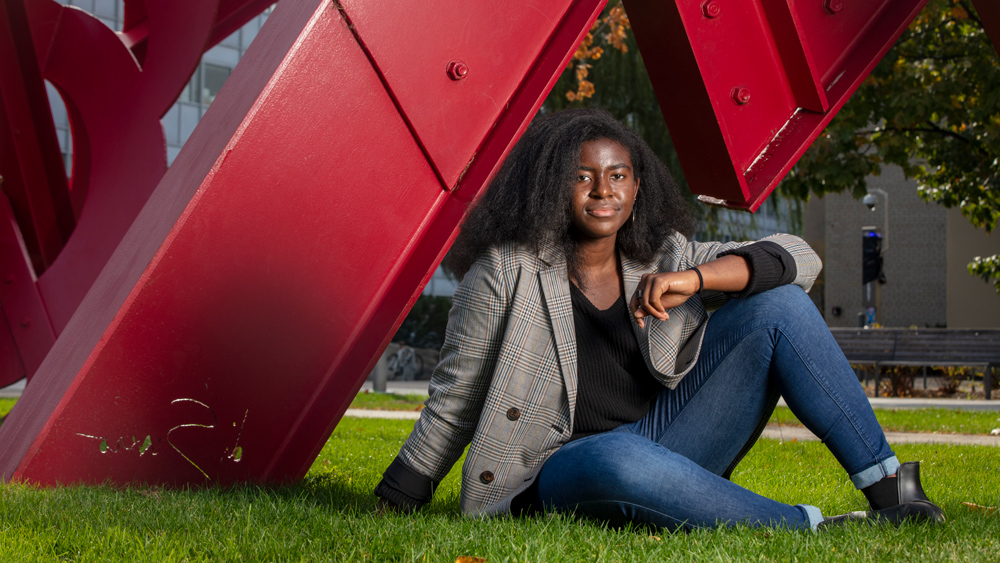 MIT senior Amanda Orji sitting under a red metal sculture on the grounds of MIT