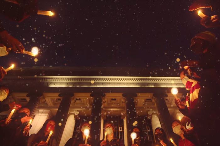 Screenshot showing group of MIT community with candles in front on Killian Court
