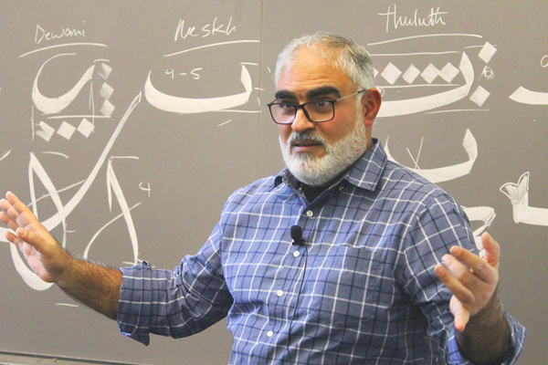 Hajj Wafaa standing in front of a board covered in Arabic caligraphy