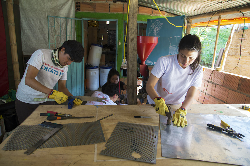 Two students wearing gloves use a hammer and measuring tools while working with materials during study abroad in Bogota, Colombia.