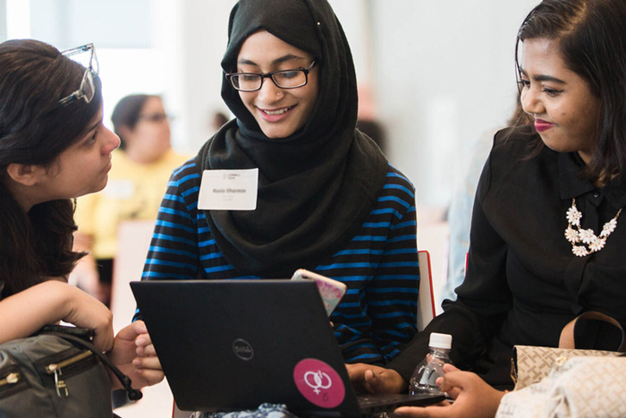 3 people chat at an event, with one using a laptop 
