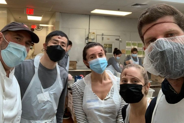 A group of women and men in a kitchen wearing aprons and face masks