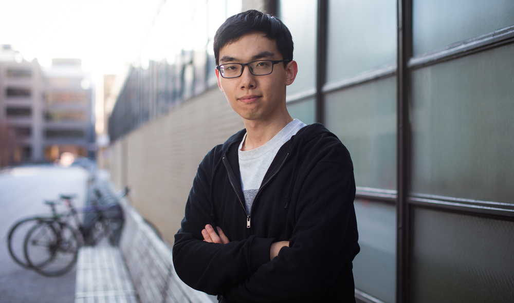 Changhao Li outside on campus with buildings and bikes in background