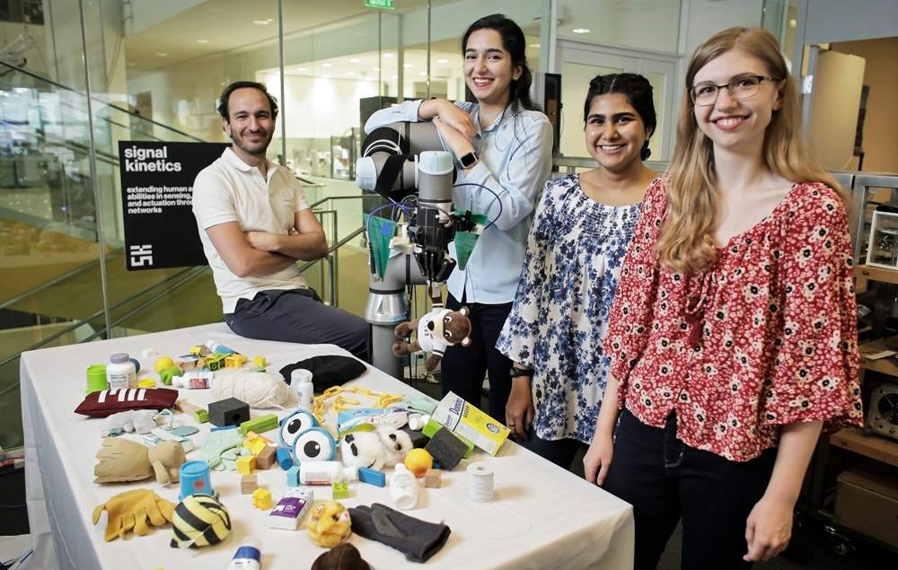 Four researchers in the lab standing by a robotic arm and various items on a table