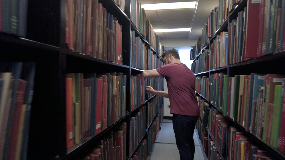 An MIT staffperson cleans a library book shelf
