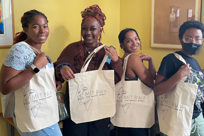 4 members of the MIT Black Women’s Alliance pose with a new BWA bag with a stylized profile on it