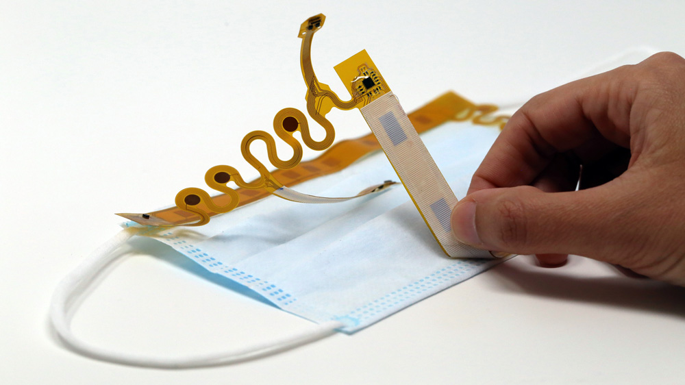 a blue paper face mask with an interior sensor being manipulated by a person's hand