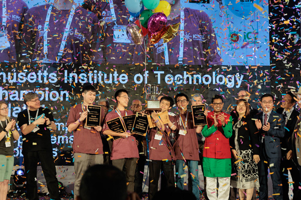 A group of MIT student coders celebrating on stage while people around them applaud