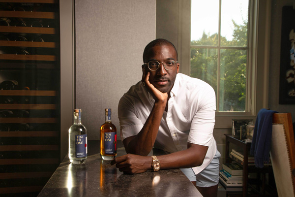 Marc-Kwesi Farrell leaning on a table that has 2 bottles of Ten To One rum on it