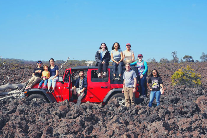 10 people pose for photo outside, some sitting on red jeep
