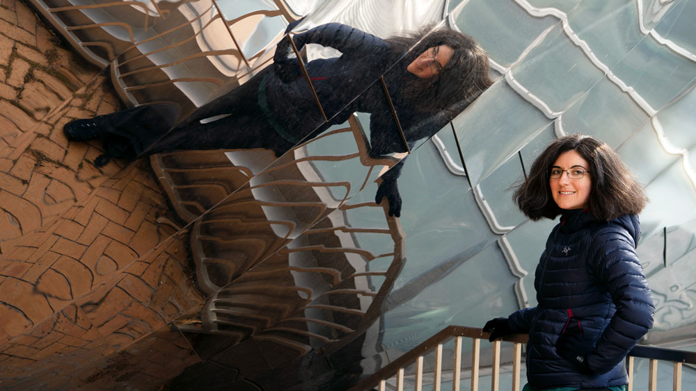 Tamara Broderick stands outside the Stata Center and its reflective façade fills the background. Her reflection spreads dramatically across the photo.