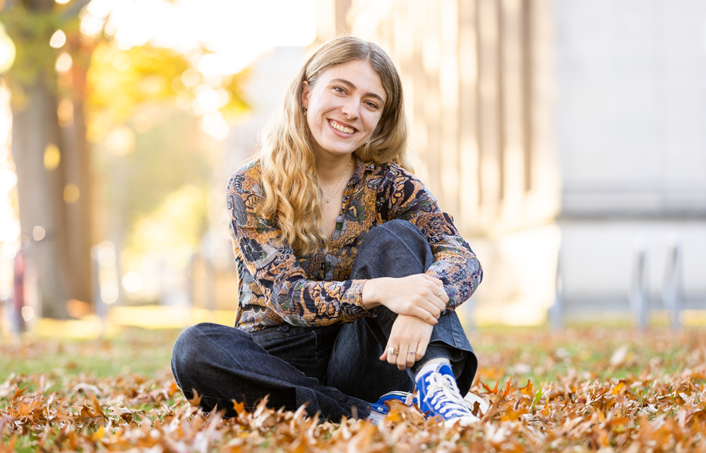 Aviva Intveld smiles while outside sitting on MIT campus lawn, with fall leaves.