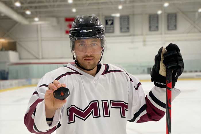 MIT hockey player in rink holds a small black device