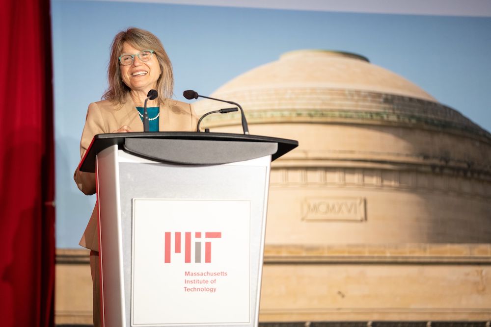 Sally Kornbluth stands behind a lectern with the MIT logo. An image of the Great Dome is behind her.