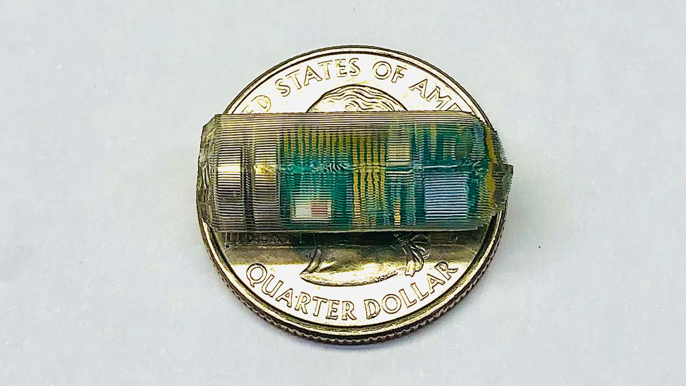 The tiny transparent pill sits on a quarter and is about the same length as the quarter’s diameter.