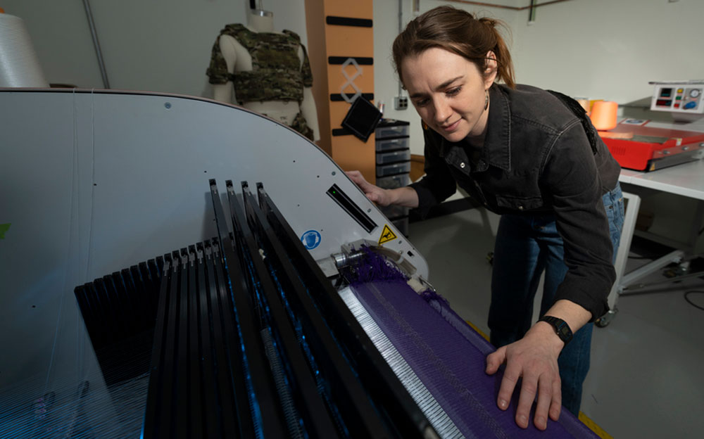 A person inspects a unique loom-like fabric printer, brushing their hand over the threads in this fish-eye lens photo