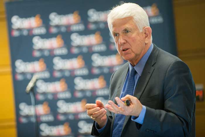Bob Metcalfe speaks at an event, with blurry banner in background