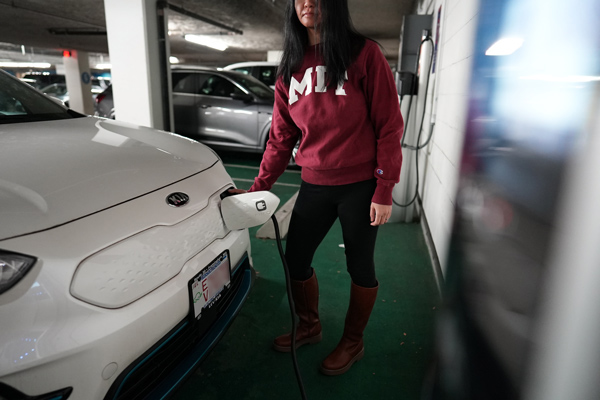 A person wearing an MIT shirt charges their electric vehicle in an indoor parking lot. 