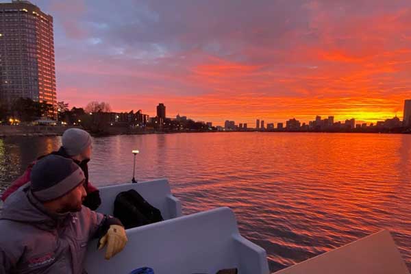 2 MIT crew members look at the bright orange sunset over the Charles river