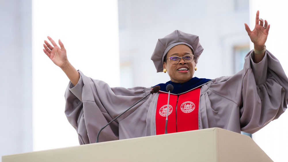 Chancellor Melissa Nobles in academic regalia speaking at a podium with her arms raised 