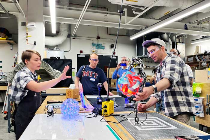 Rober in a busy lab with MIT community members, holding spherical brightly colored objects