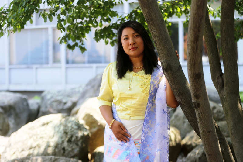 Rani Ukhengching Marma is outside with her hand resting on a tree, with the rocky Stata Center Swale and the Whitaker Building in background.