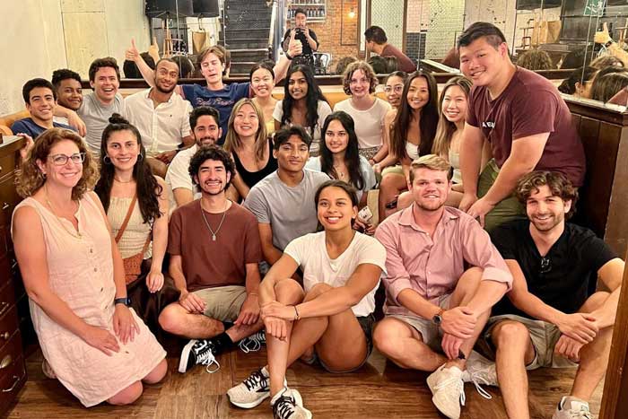 About 25 interns smile for a group photo indoors, with some sitting on the floor