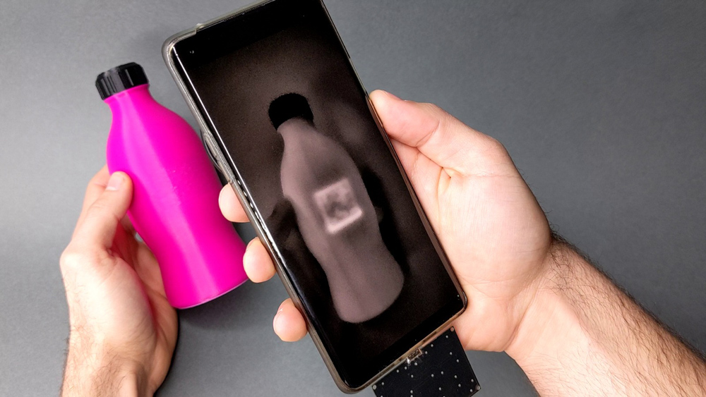 A cellphone takes a photo of a pink water bottle, and a hidden square tag on the bottle appears on the phone's screen