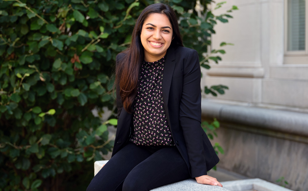 Avni Singhal sits outside on MIT campus and smiles. A peek of an MIT building is in the background.