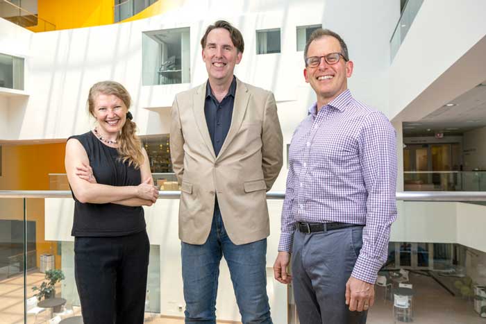 Ev Fedorenjo, Edward Gibson, and Roger Levy pose together, standing on a walkway overlooking an atrium
