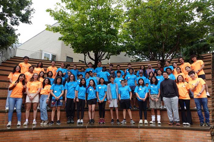 About 50 dynaMIT and MIT students wearing matching blue or orange T-shirts pose in three rows on the steps of the Stata Center