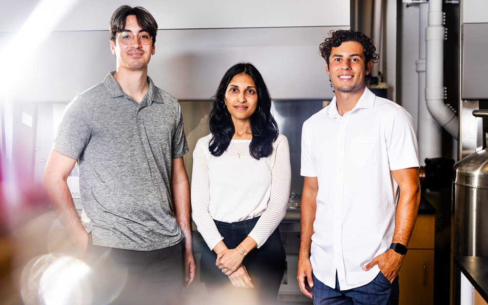 Left to right: Angel Bu, Ritu Raman, and Brandon Rios stand in the lab, with blurry light in foreground.