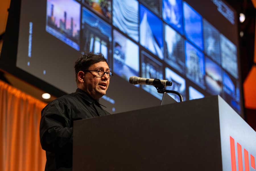 Refik Anadol speaks at podium with colorful projection in background